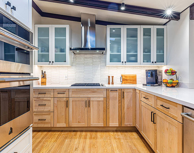 The image shows a modern kitchen interior with light wood cabinets, stainless steel appliances, white countertops, and a hardwood floor.