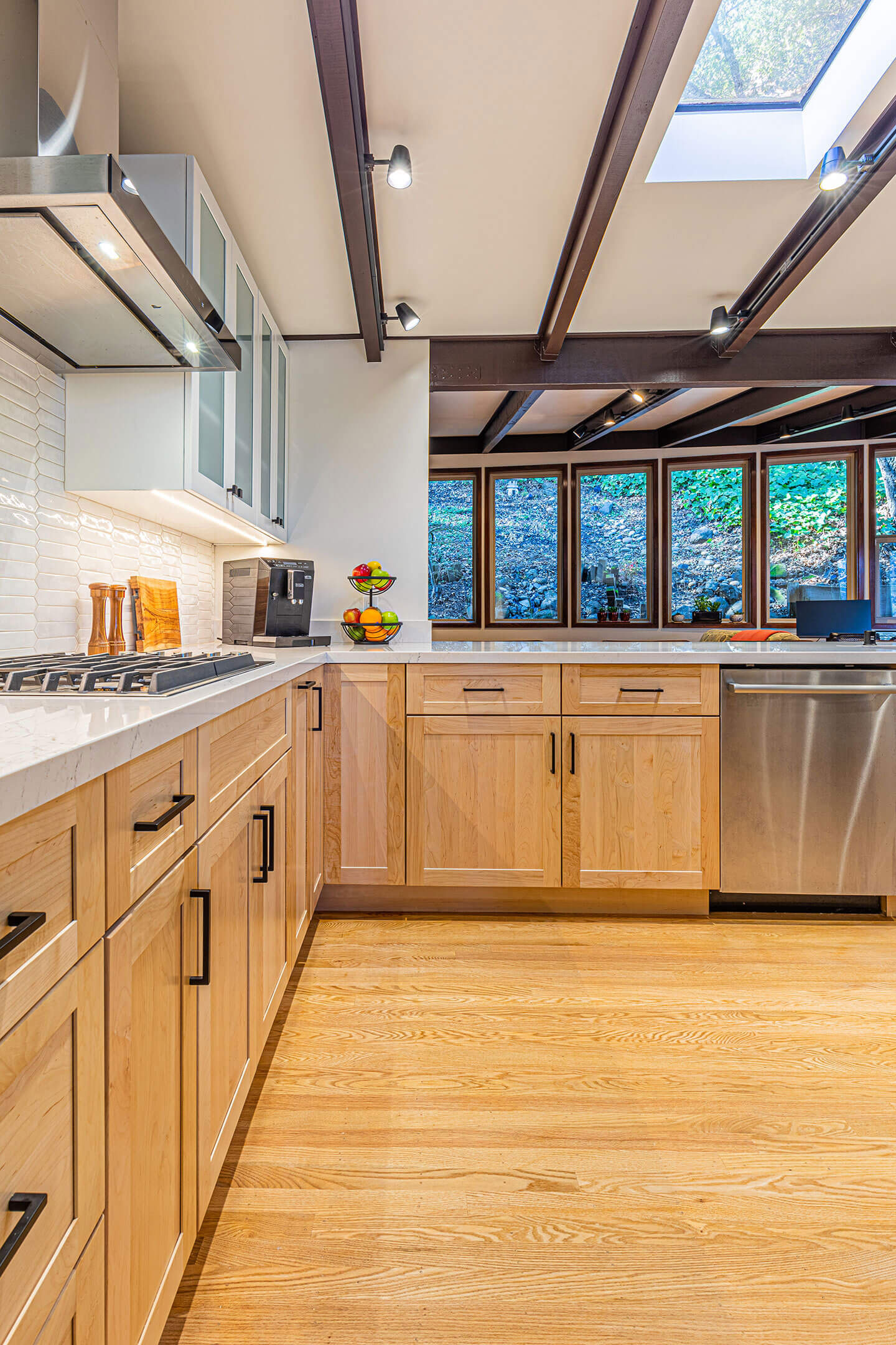 The image shows a modern kitchen interior with wooden cabinets, stainless steel appliances, hardwood flooring, and recessed lighting.