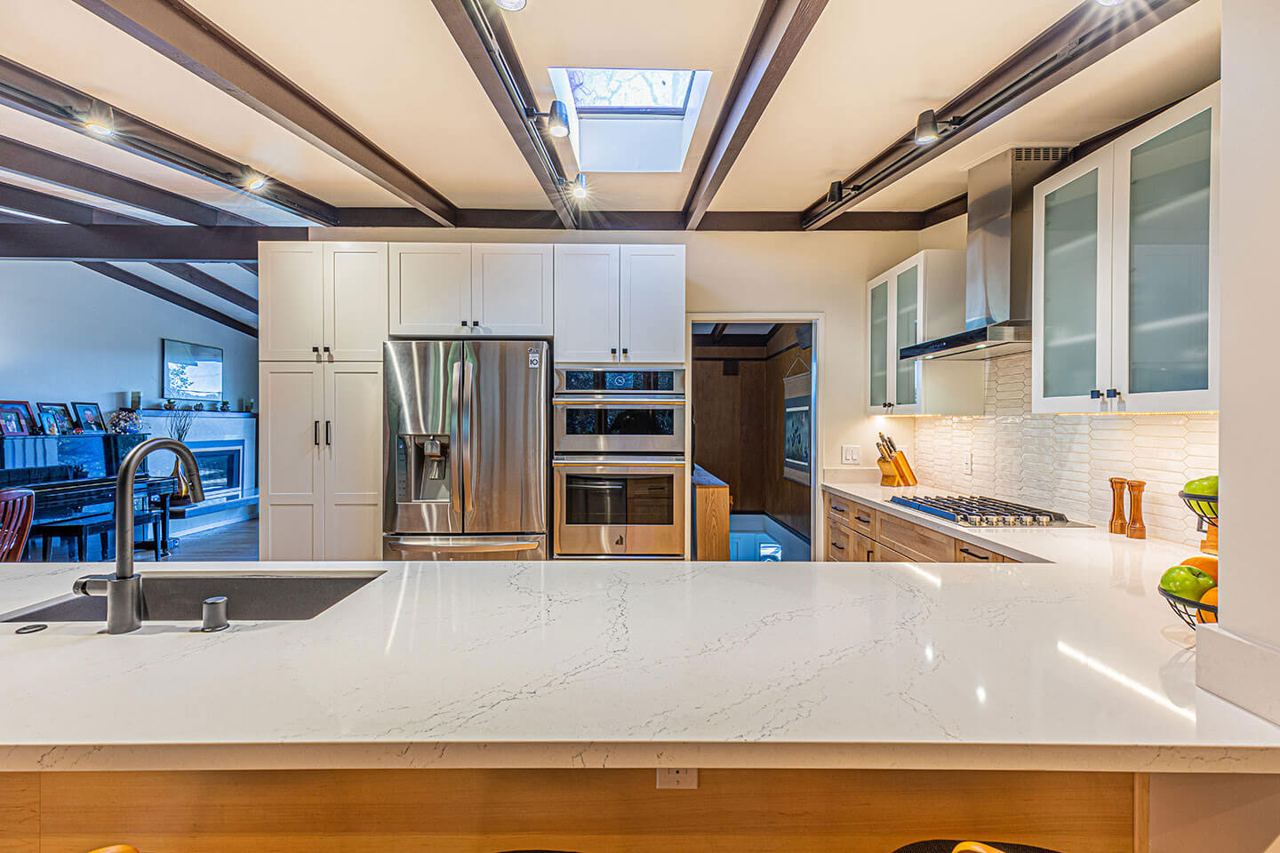 The image shows a modern kitchen interior with a large island countertop, stainless steel appliances, white cabinets, and a clean, minimalist design.