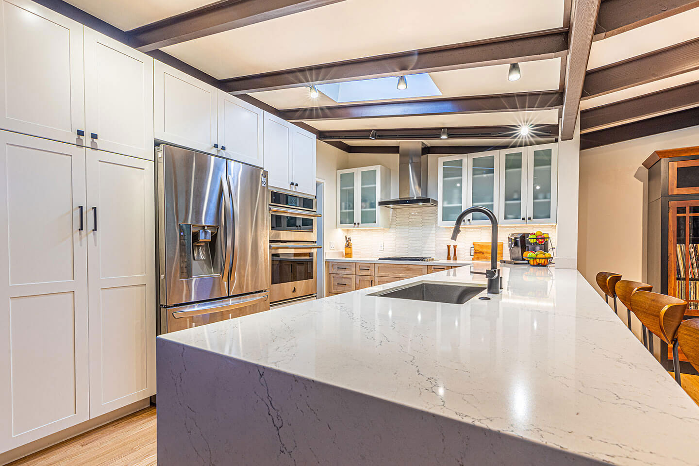 The image shows a modern kitchen with a large island countertop featuring a marble surface, stainless steel appliances, white cabinets, and a contemporary design.