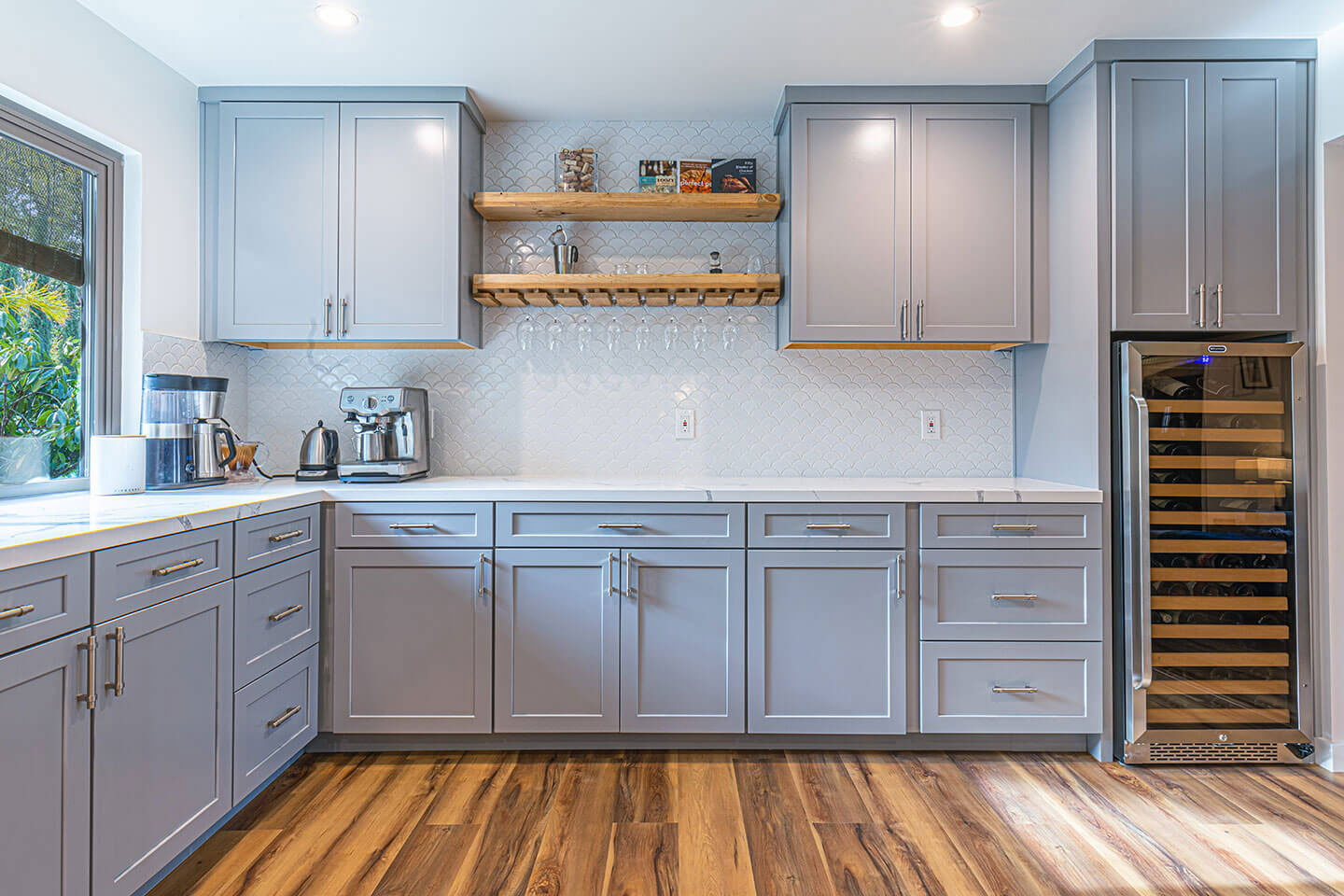 A modern kitchen with gray cabinets, stainless steel appliances, a wooden floor, and a white backsplash.