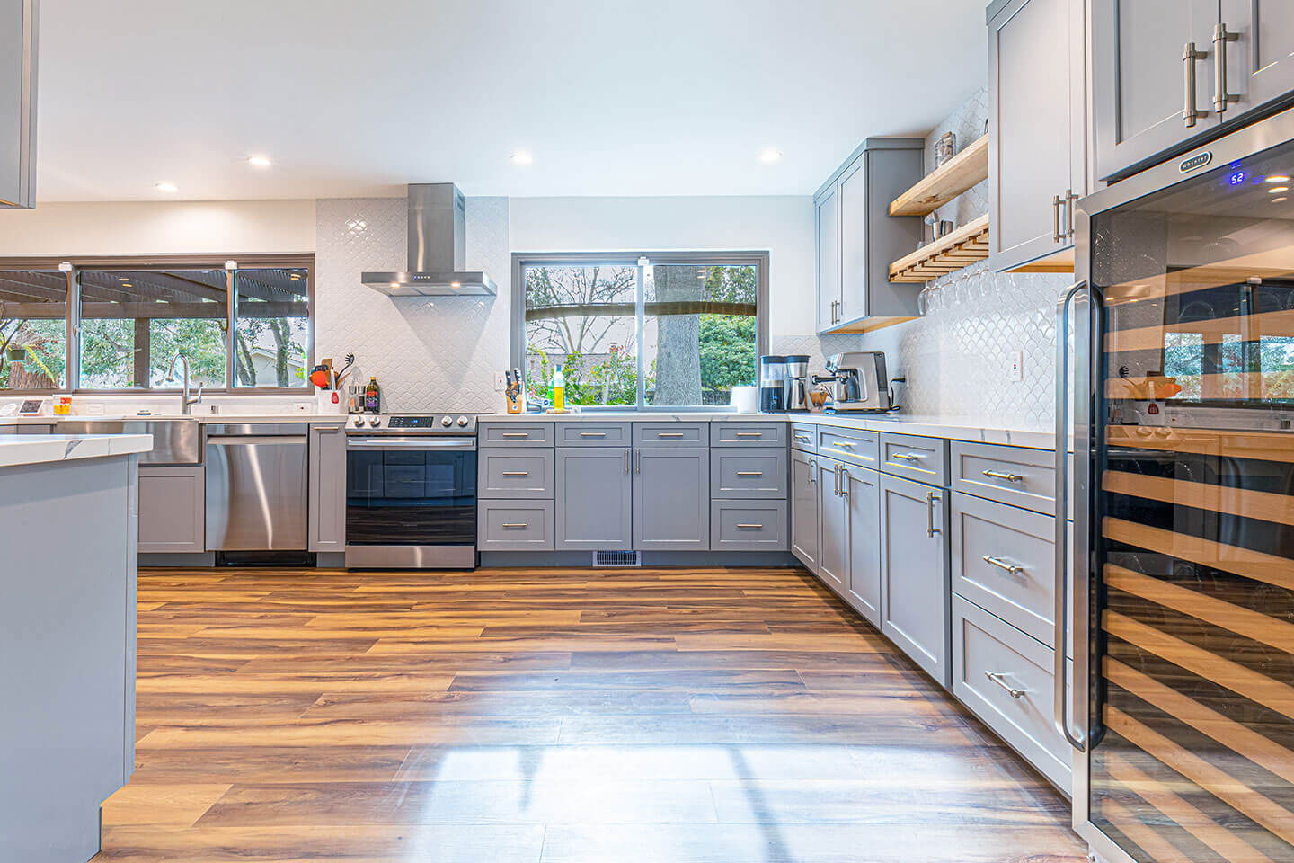 A modern, well-lit kitchen with stainless steel appliances, wooden flooring, and a large island with a sink.
