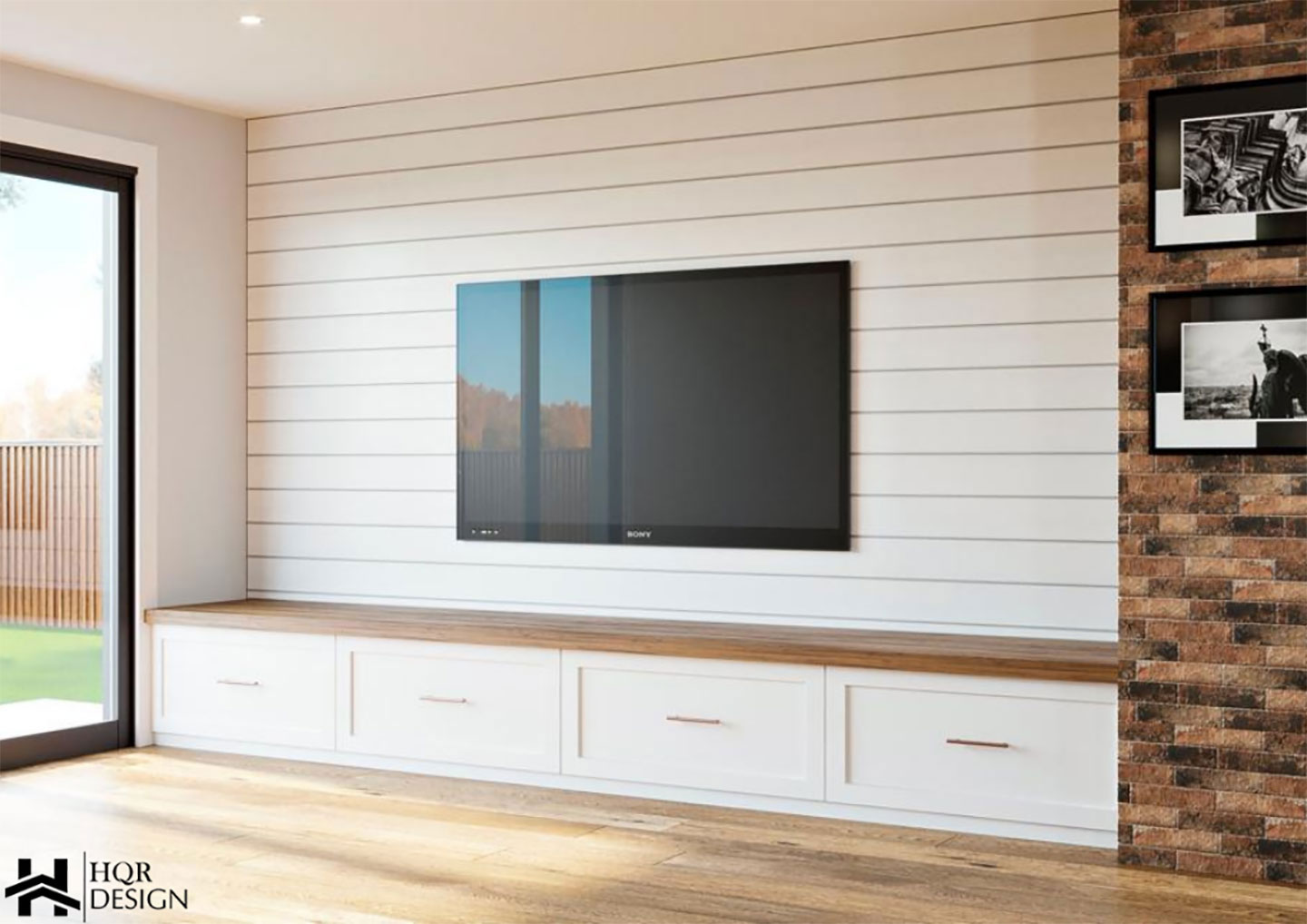 The image shows a modern living room with a large flat-screen television mounted on a white wall above a wooden bench, set against a brick wall backdrop.