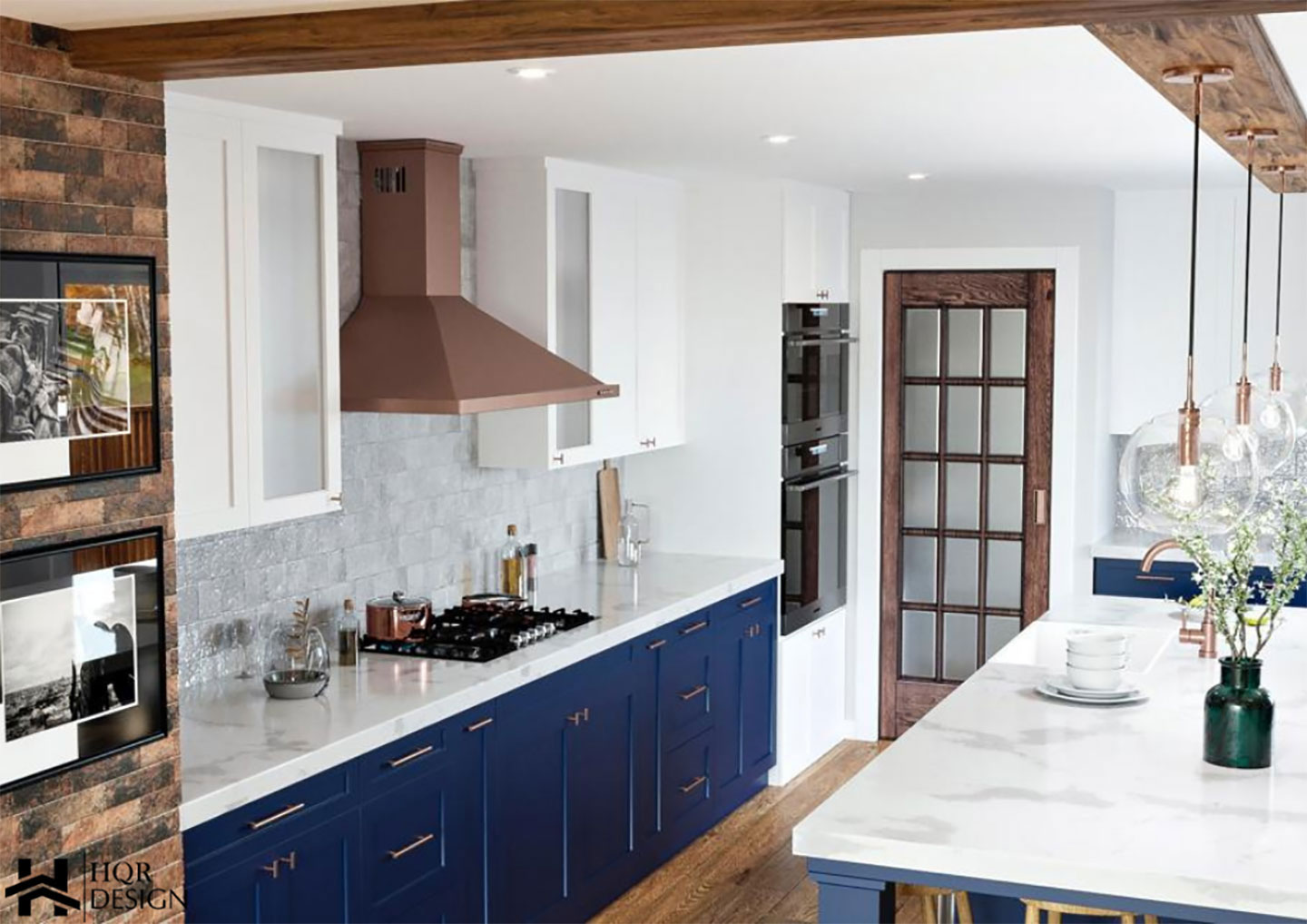 The image shows a modern kitchen interior with blue cabinets, marble countertops, stainless steel appliances, and a brick wall feature.