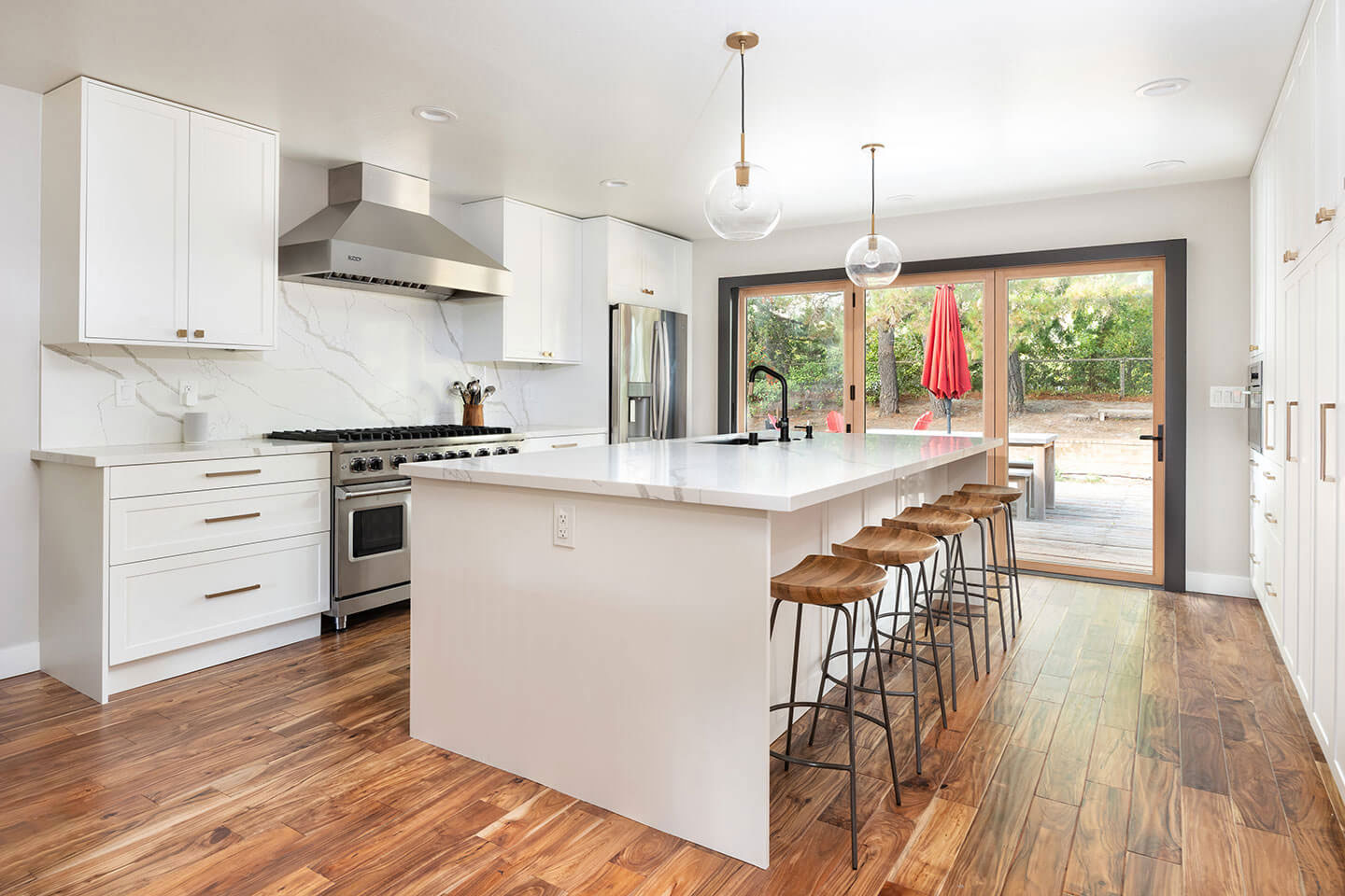 A modern kitchen with white cabinets, dark hardwood flooring, stainless steel appliances, and a center island with bar stools.