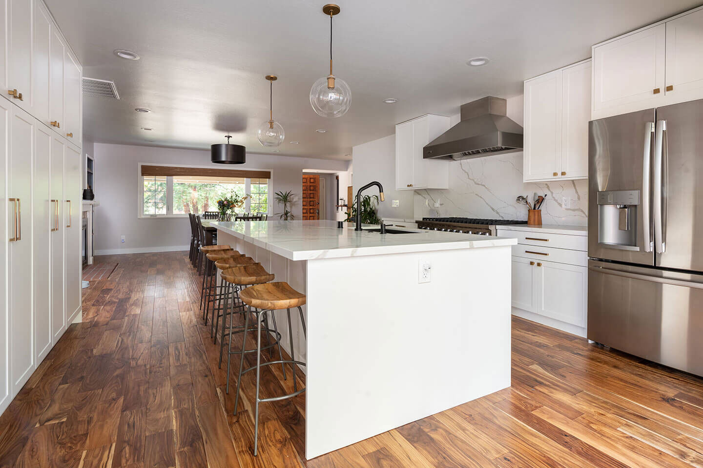 A modern kitchen with white cabinets, stainless steel appliances, hardwood flooring, and wooden furniture.