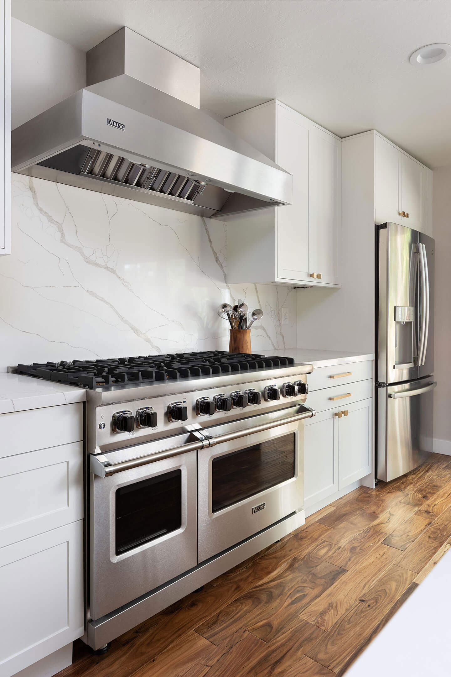 A modern kitchen with stainless steel appliances, white cabinets, marble backsplash, and hardwood flooring.
