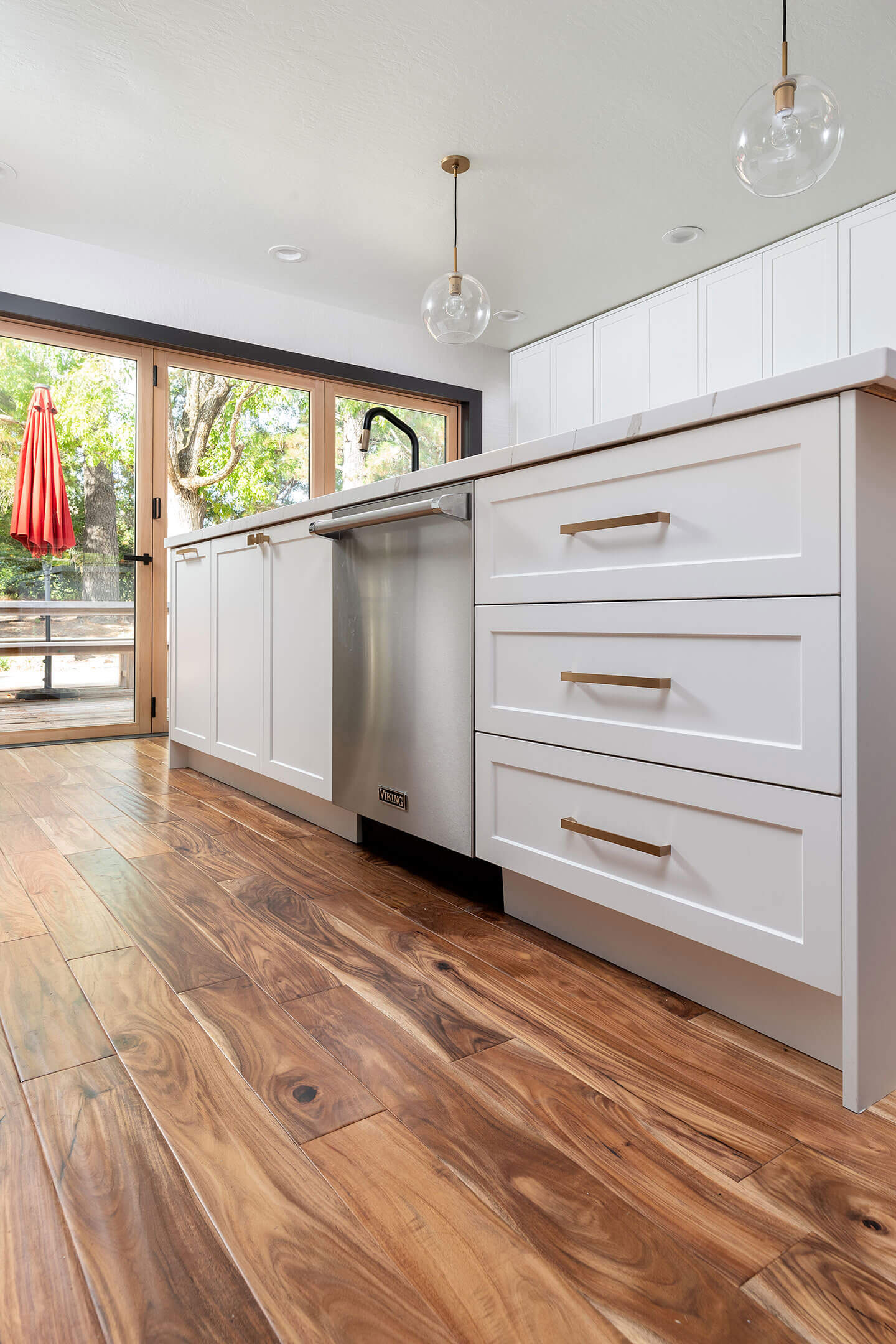 The image shows a modern kitchen interior with a white cabinetry, stainless steel appliances, hardwood flooring, and a large island in the center.
