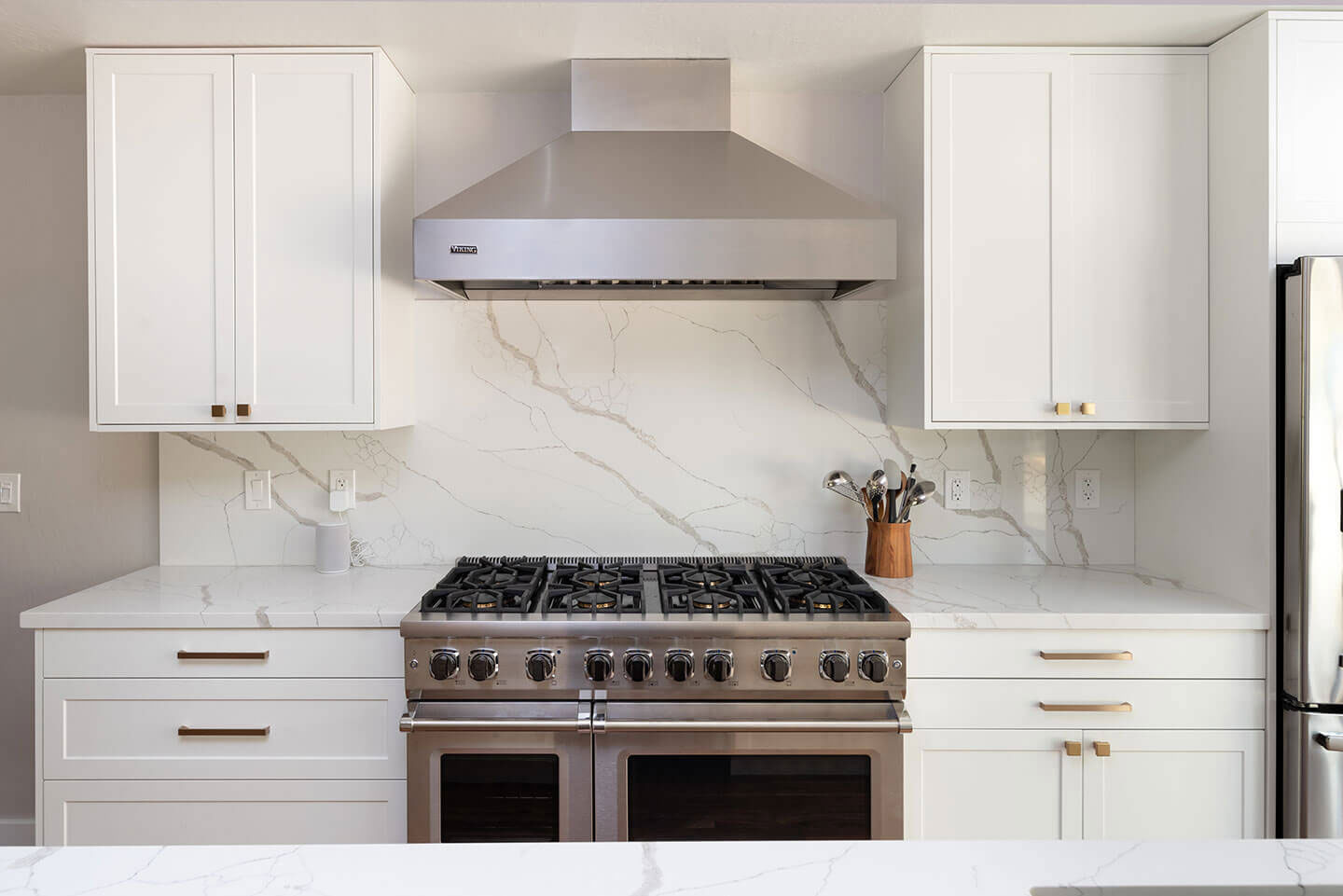 A modern kitchen with white cabinets, marble backsplash, stainless steel appliances, and a large island with a gas stove.