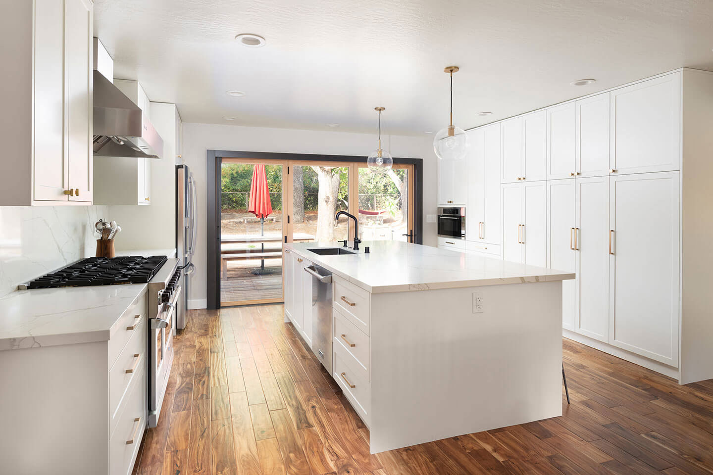 The image shows a modern kitchen interior with white cabinets, hardwood flooring, stainless steel appliances, an island countertop, and a clean, well-lit space.